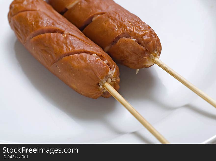 Two sausages on the white dish, serve with wooden stick