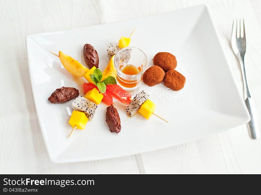 A fine fruit salad dessert on white plate with chocolate truffles and caramel sauce. A fine fruit salad dessert on white plate with chocolate truffles and caramel sauce.