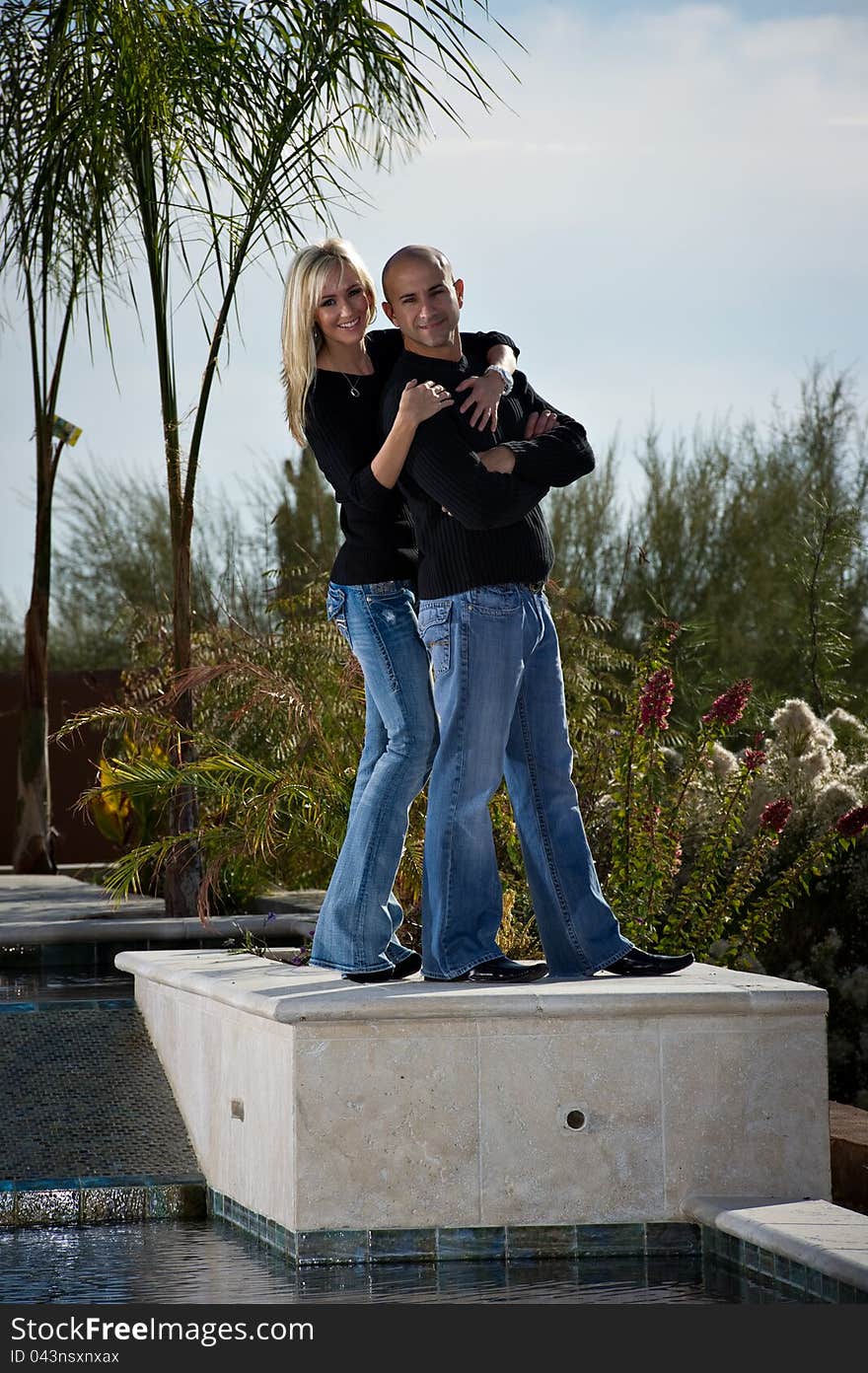 Full length of a happy playful couple posing next to a pool. A green winter desert landscape is in the background. Full length of a happy playful couple posing next to a pool. A green winter desert landscape is in the background.