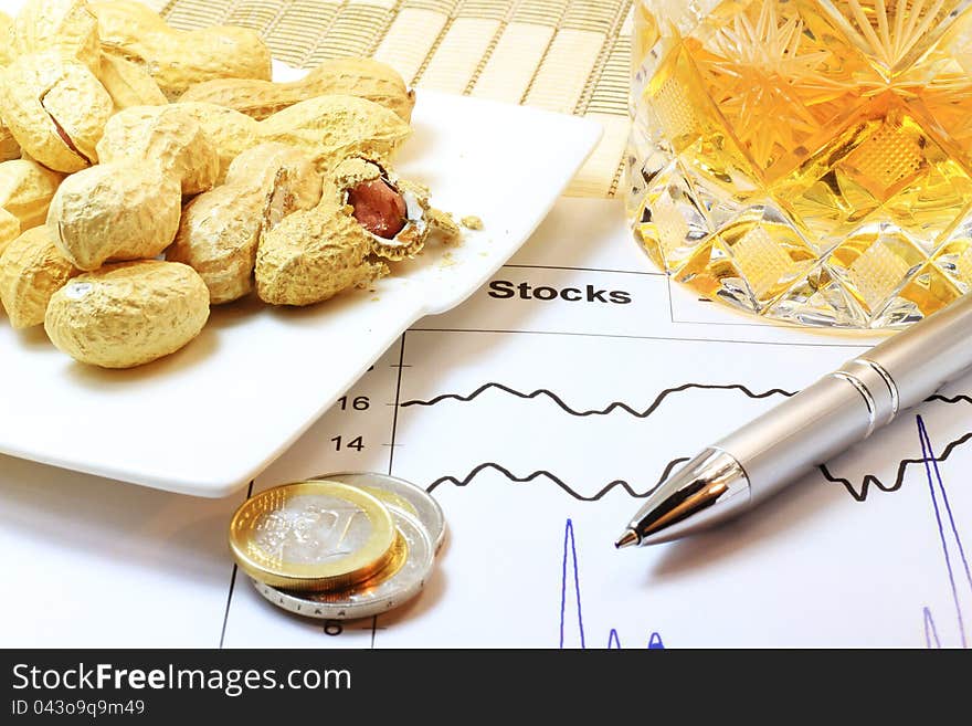 A concept of stock market, crisis and gambling with money; peanuts, coins, drink, a pen and stock graph on the table. A concept of stock market, crisis and gambling with money; peanuts, coins, drink, a pen and stock graph on the table.