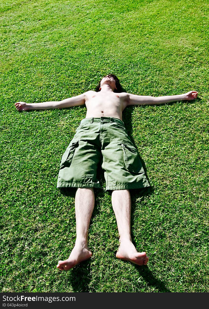 The young man has a rest on a grass having stretched hands