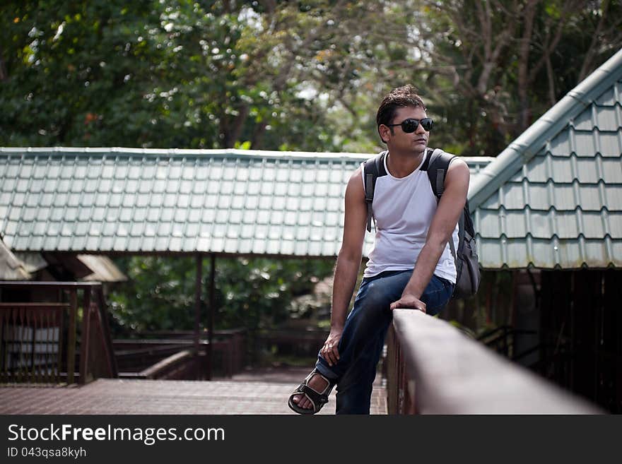 Indian Happy young man sitting on railing of house with sunglasses. Indian Happy young man sitting on railing of house with sunglasses