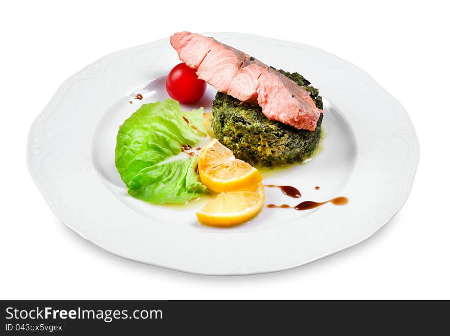 Salmon with spinach garnish, cherry tomato, lemon slices on a plate, on white