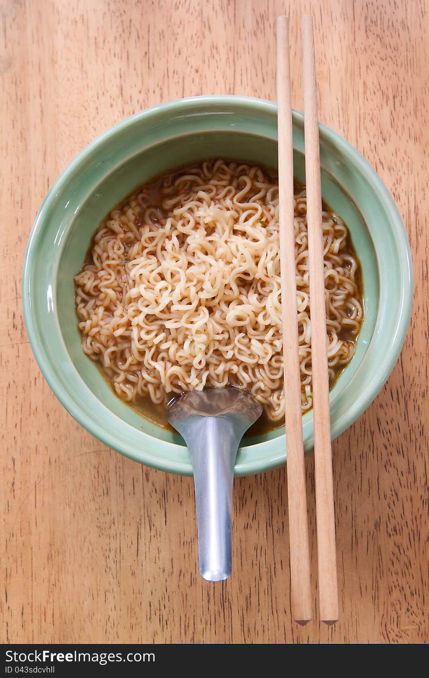 Instant noodle with spoon and chopsticks in a ceramic bowl on wood background