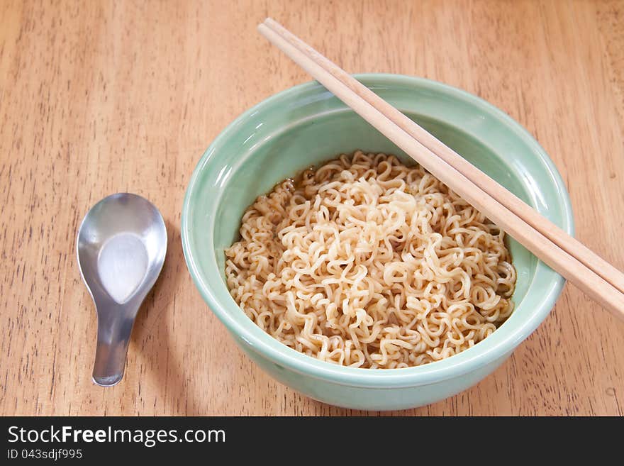 Instant noodle with spoon and chopsticks in a ceramic bowl on wood background