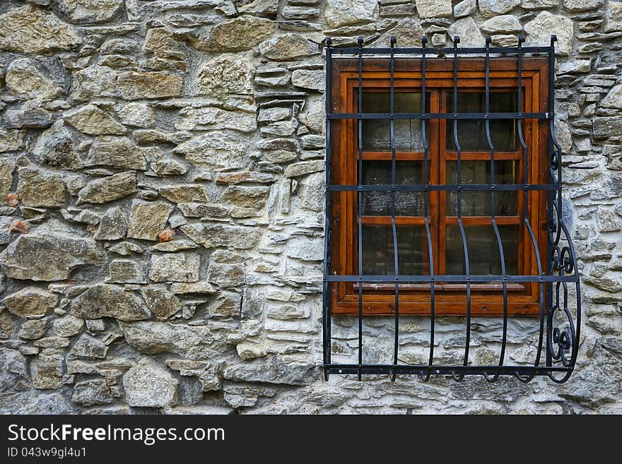 Stone wall with window enclosed in wooden frame and steel ornamental grillage on it. Stone wall with window enclosed in wooden frame and steel ornamental grillage on it