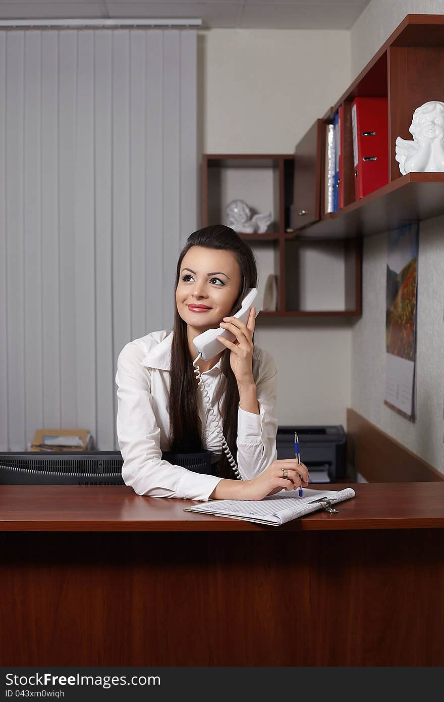 Happy young smiling businesswoman sitting at the table in office meeting room, talking on phone and writing. Happy young smiling businesswoman sitting at the table in office meeting room, talking on phone and writing