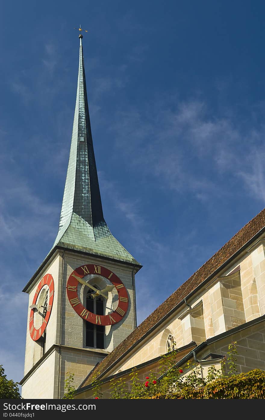 Green steeple on a short clock tower against a blue sky, also showing part of the roof of the church. Green steeple on a short clock tower against a blue sky, also showing part of the roof of the church