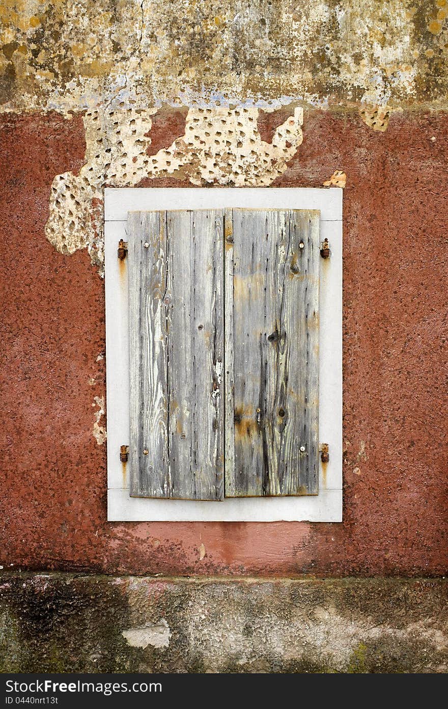 Rusty closed woodn window with white border made of sotne. Wall has nice read texture. At the top are visible marks of broken roughcast. . Rusty closed woodn window with white border made of sotne. Wall has nice read texture. At the top are visible marks of broken roughcast. .