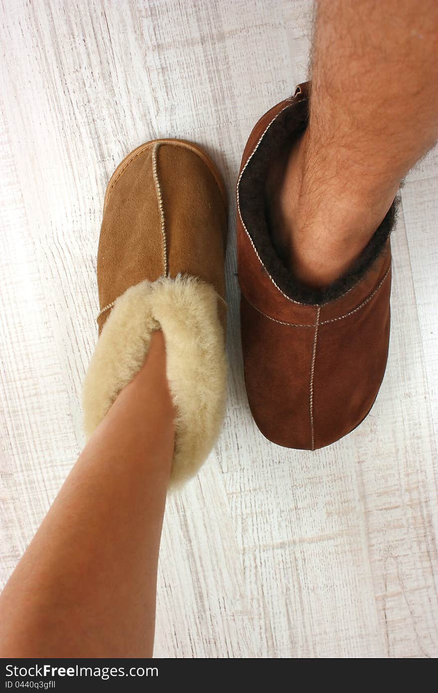 A male and female feet ware warm slippers on a white floor. A male and female feet ware warm slippers on a white floor
