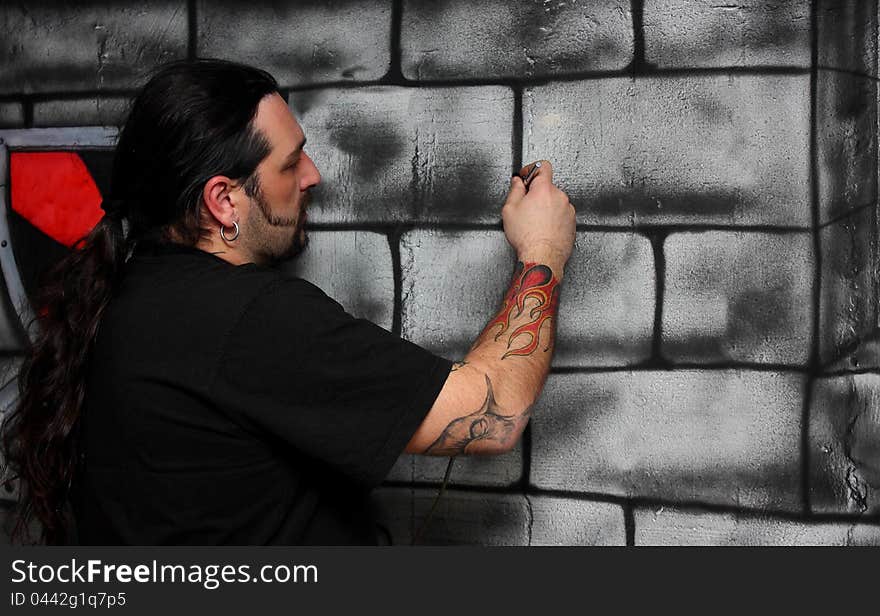 A man with tattoos make drawing on a wall painting bricks. A man with tattoos make drawing on a wall painting bricks