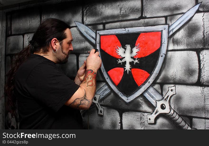 A man with tattoos make drawing on a wall painting knight shield. A man with tattoos make drawing on a wall painting knight shield