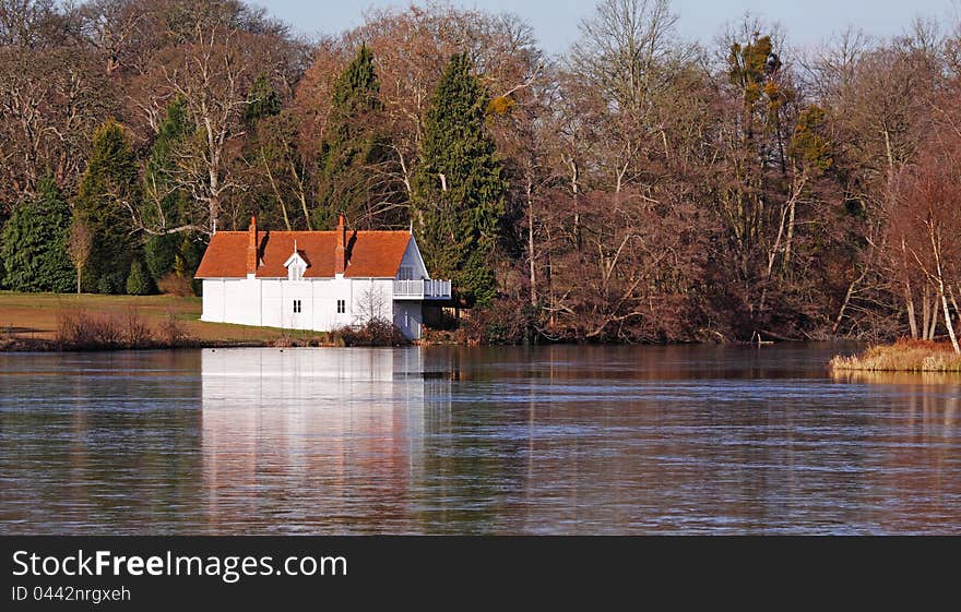 Whitewashed Lakeside Boathouse bathed in Winter sunshine with Woodland behind. Whitewashed Lakeside Boathouse bathed in Winter sunshine with Woodland behind