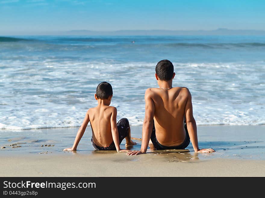 Two brothers relaxing at the water's edge after a fun day of playing at Huntington Beach. Two brothers relaxing at the water's edge after a fun day of playing at Huntington Beach.