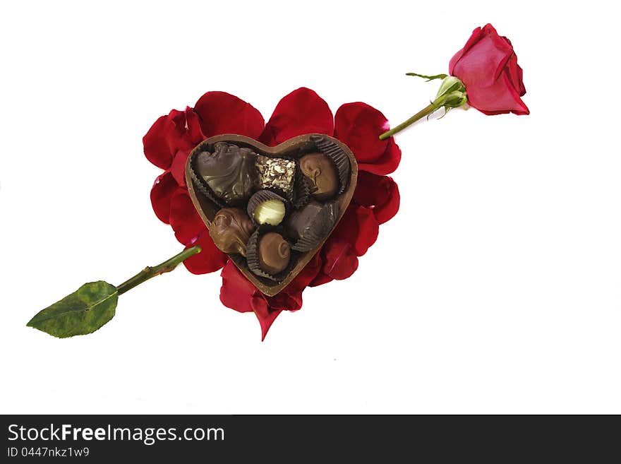 Photo of Fancy chocolates in a chocolate heart shaped container arranged on a heart-shaped bed of red rose petals with a piercing rose arrow. Photo of Fancy chocolates in a chocolate heart shaped container arranged on a heart-shaped bed of red rose petals with a piercing rose arrow