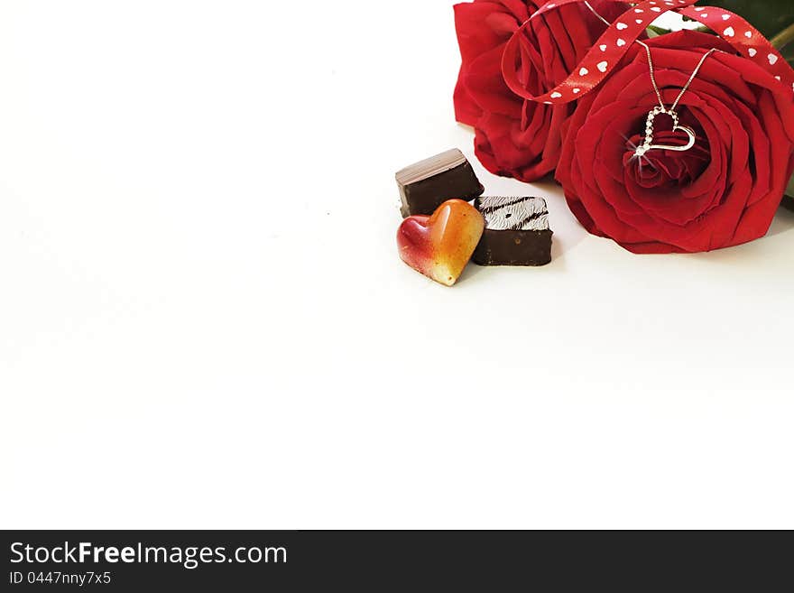 A still life composition of a White Gold and Diamond necklace hanging from a red rose with fancy chocolates on the foreground and lots of copy space. A still life composition of a White Gold and Diamond necklace hanging from a red rose with fancy chocolates on the foreground and lots of copy space.