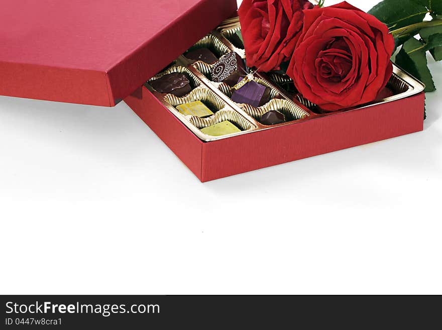 A Still life composition of a gold diamond engagement ring with a red box of fancy chocolates and red roses. A Still life composition of a gold diamond engagement ring with a red box of fancy chocolates and red roses