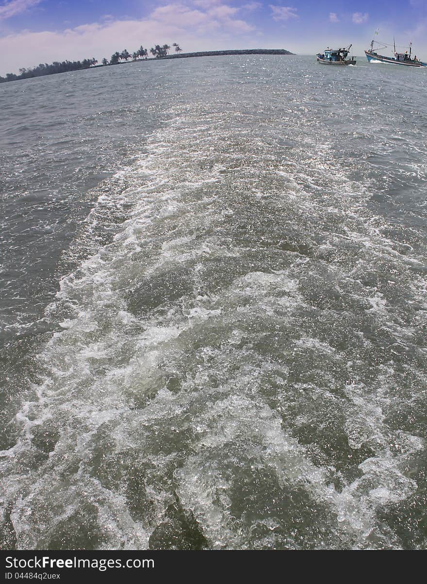 Wake or trail from a boat in arabian sea with fishing boats and shore visible in the backdrop. Photo taken near Udupi, Karnataka, India