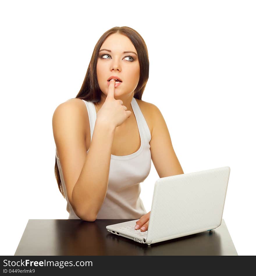 The young woman thinks with the laptop behind a table on a white background. The young woman thinks with the laptop behind a table on a white background