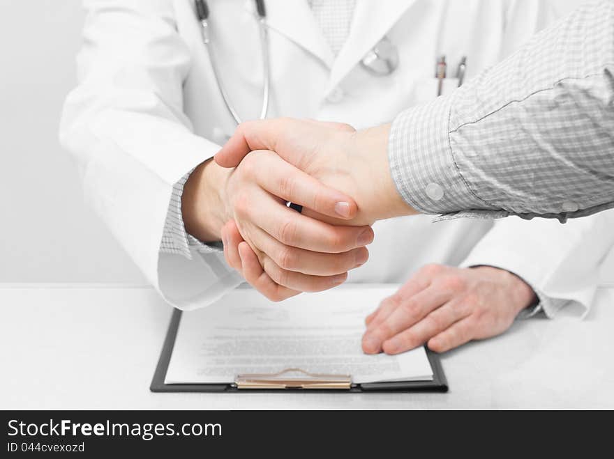 Doctor with stethoscope and clipboard shaking patients hand