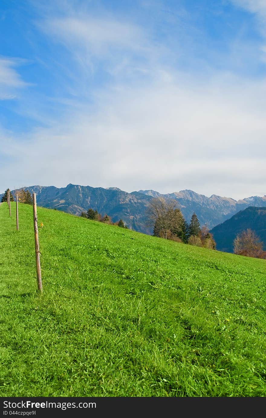 Alps meadow with light fence and blue sky background