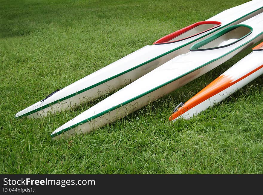 Three colourful K1 sprint kayaks with long pointy beams lying on green grass. Three colourful K1 sprint kayaks with long pointy beams lying on green grass