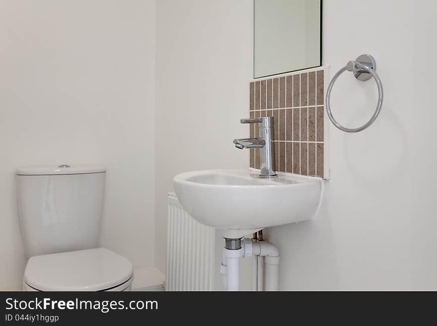 Basic cloakroom suite of white porcelain WC and basin with tiled splashback