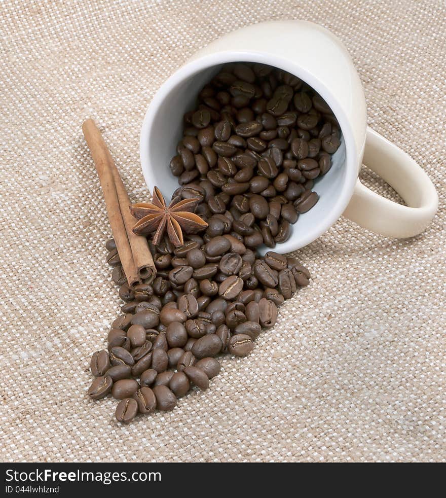 Coffee is a bob, the sticks of cinnamon and anise pour out from a mug on a background sacking