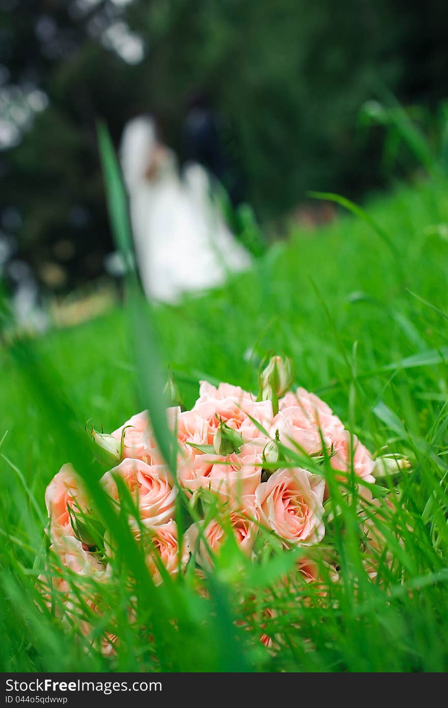 Wedding bouquet of roses laying in grass against enamoured pair
