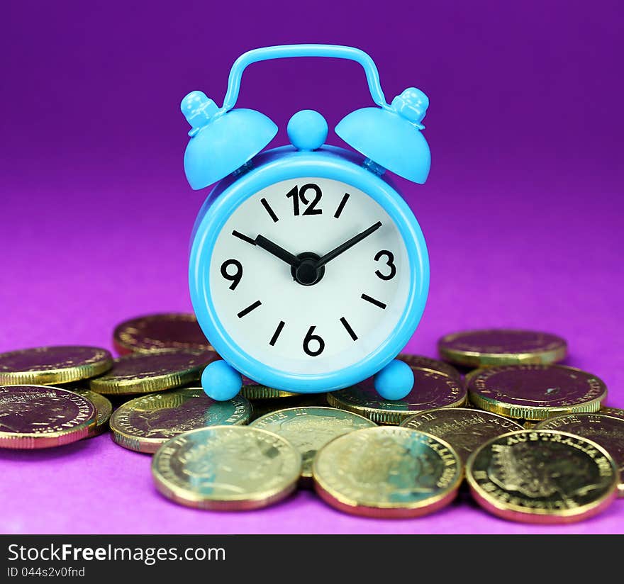 A light blue alarm clock placed on some golden coins with an orange background, asking the question how long before your investment matures?. A light blue alarm clock placed on some golden coins with an orange background, asking the question how long before your investment matures?