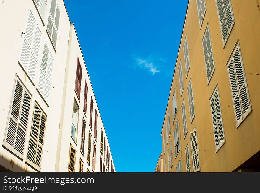 Two walls with closed windows opposite each other over blue sky