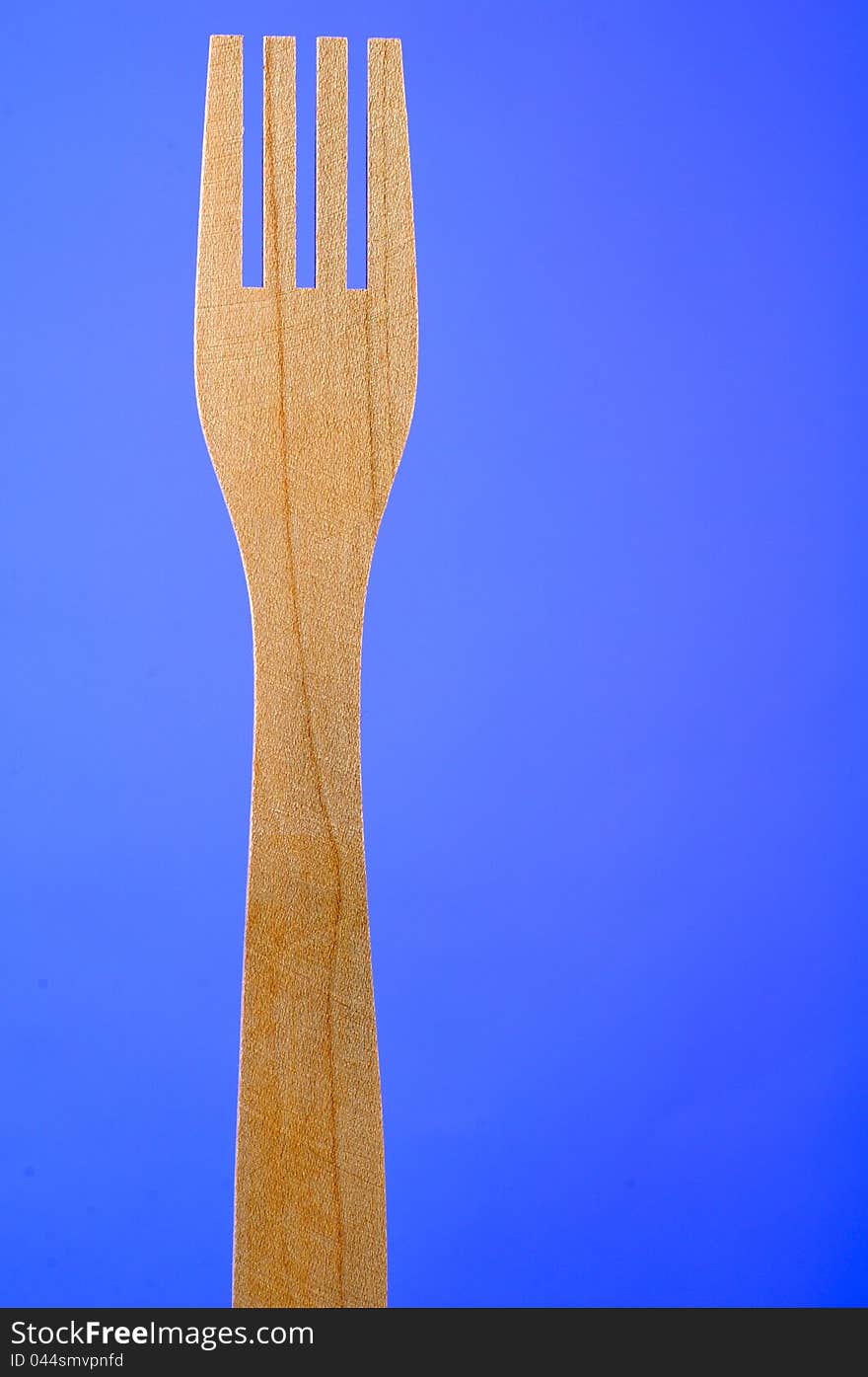 A four-pronged wooden fork on a blue background with copy space. A four-pronged wooden fork on a blue background with copy space