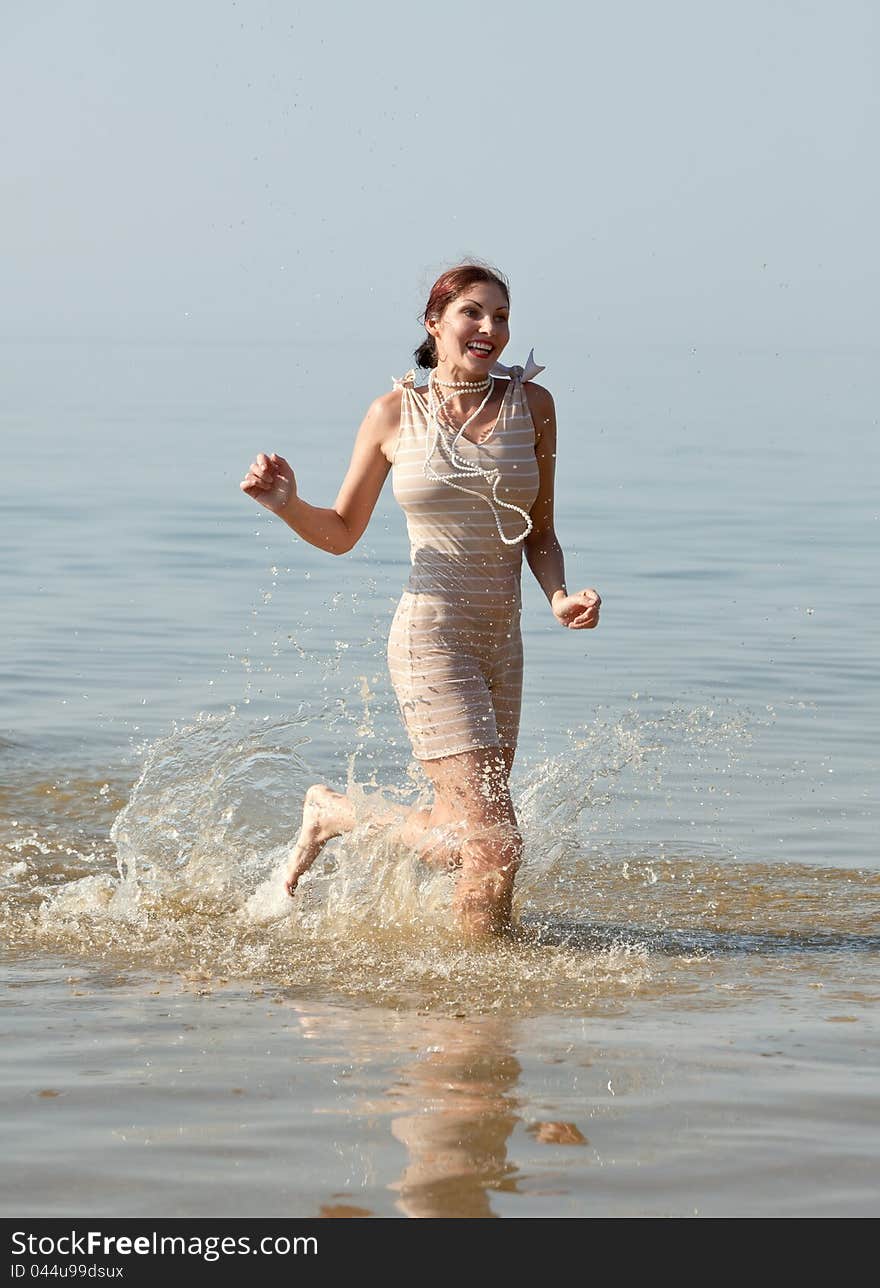 Woman in retro swimsuit smiles and runs through the water against the sea. Woman in retro swimsuit smiles and runs through the water against the sea