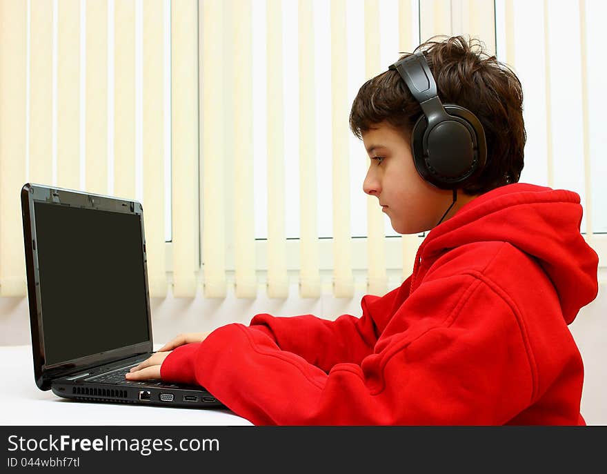 Boy working on a black laptop with headset at home (office). Boy working on a black laptop with headset at home (office)