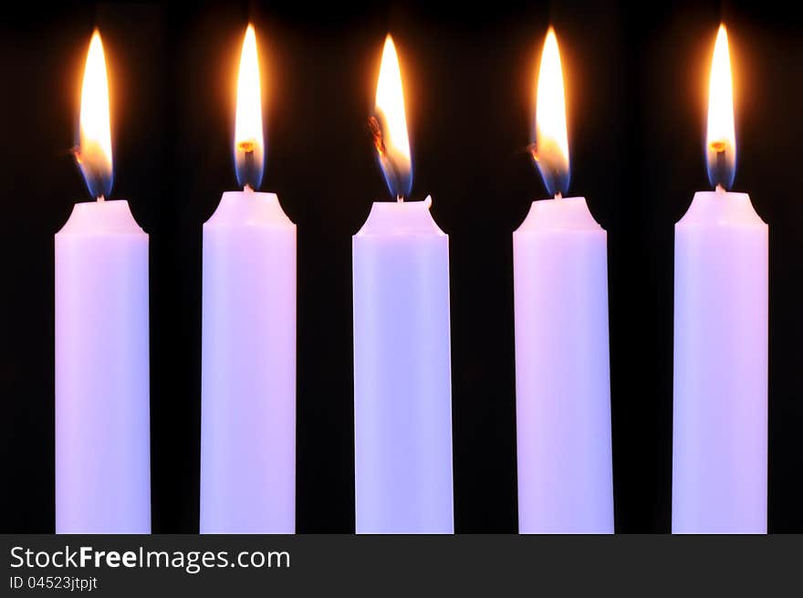 Five burning candles in a row on a black background. Five burning candles in a row on a black background