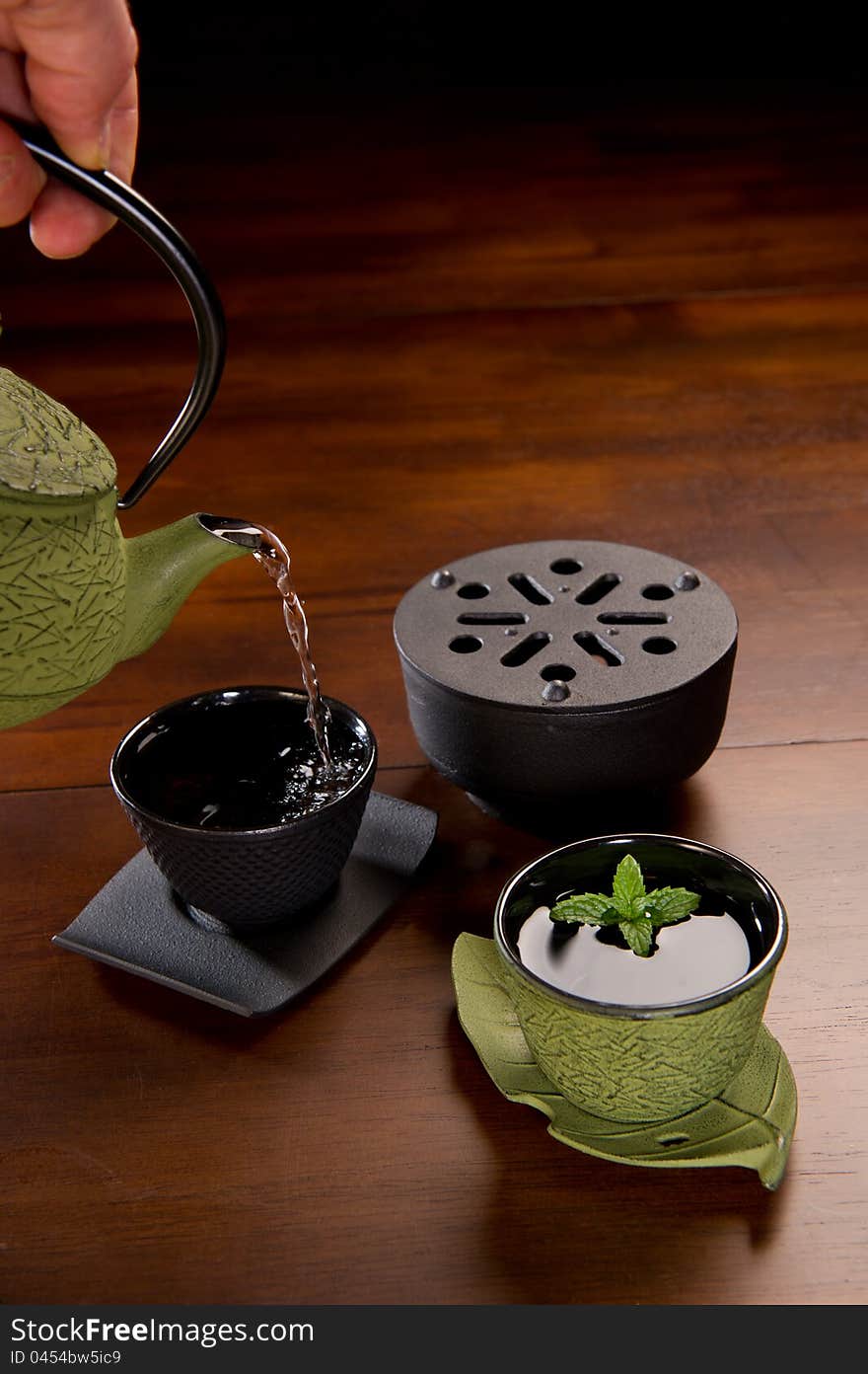 Tea being poured in a traditional Japanese cast iron tea pot and cups. Tea being poured in a traditional Japanese cast iron tea pot and cups.