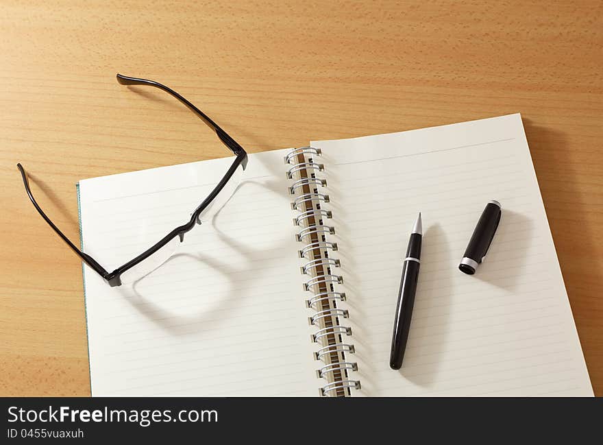 Notebook with pen and glasses on wooden table