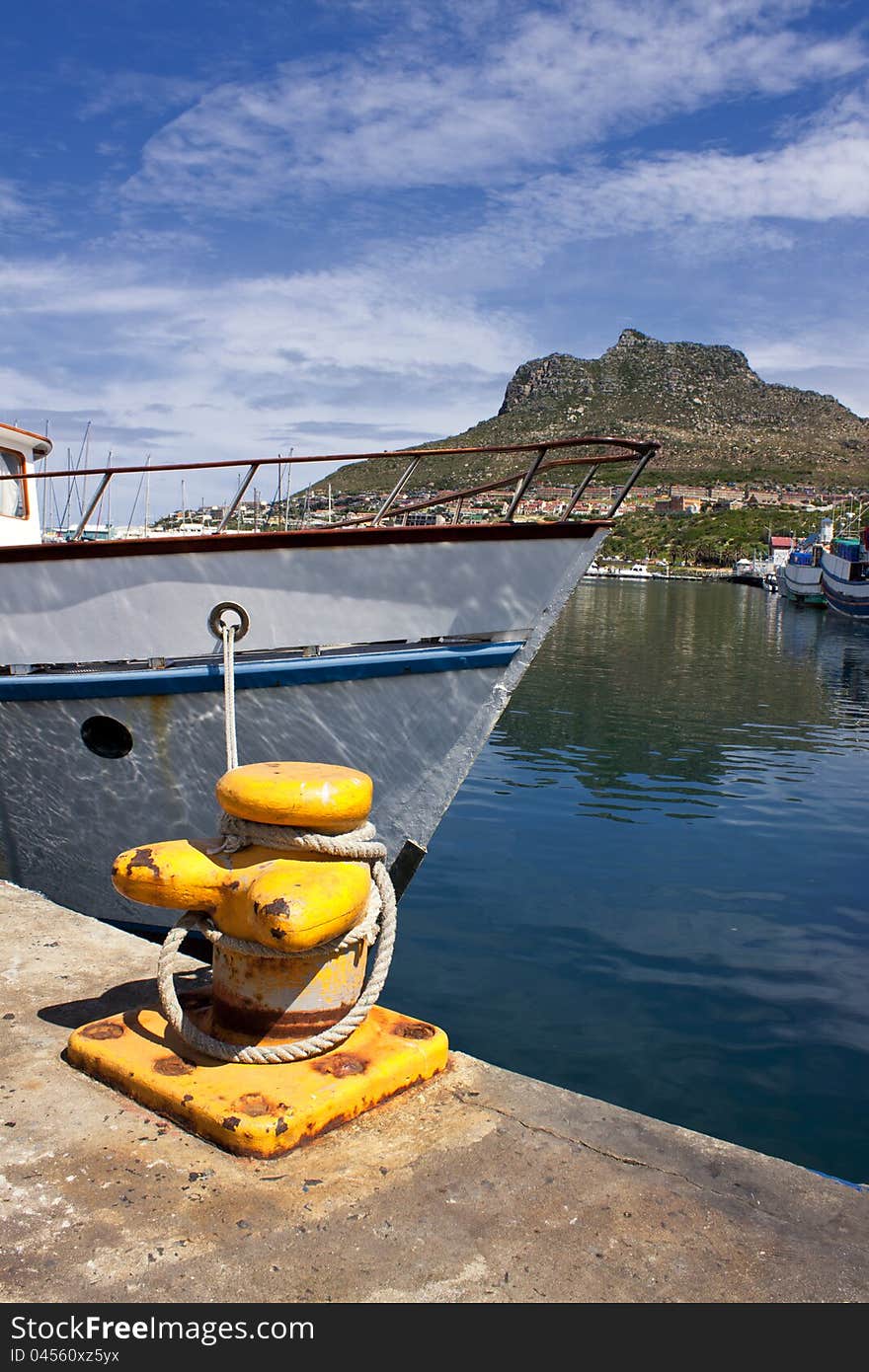 A boat moored in Houtbay Harbour, Cape Town with a mountain in the background and blue clouded skies. A boat moored in Houtbay Harbour, Cape Town with a mountain in the background and blue clouded skies