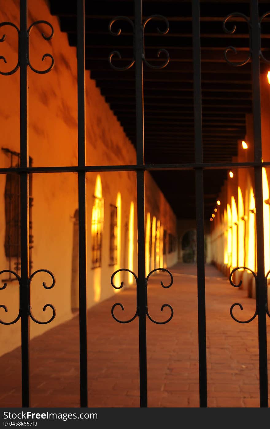 View of a long corridor at a mission with wrought iron window grates, brick floor and thick adobe walls all highlighted with evening sun. View of a long corridor at a mission with wrought iron window grates, brick floor and thick adobe walls all highlighted with evening sun