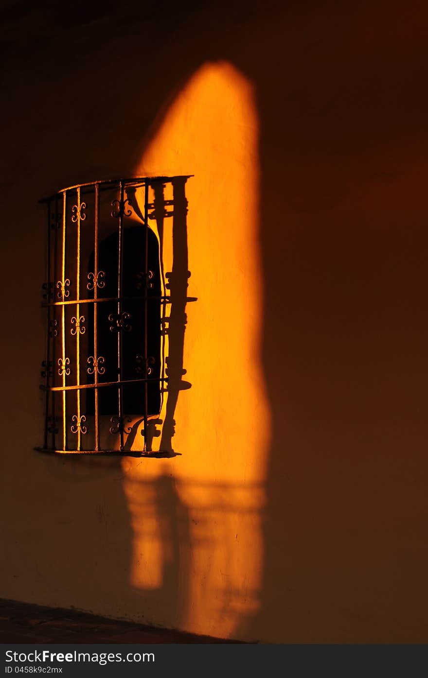 delicate wrought iron grate over a window in an adobe wall highlighted with setting sun golden light on the sdobe wall. delicate wrought iron grate over a window in an adobe wall highlighted with setting sun golden light on the sdobe wall