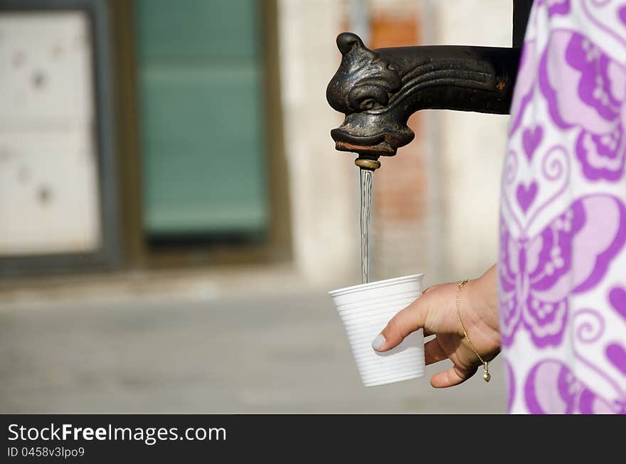 In the summer season, on a hot afternoon a girl fills plastic cup with water in the street. In the summer season, on a hot afternoon a girl fills plastic cup with water in the street