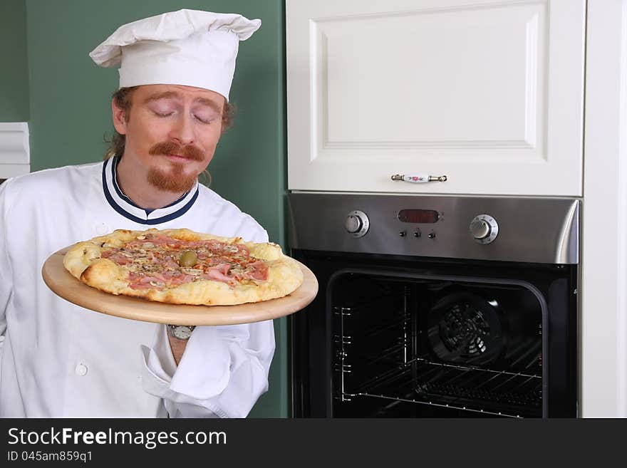 Young chef smelling italian pizza in kitchen