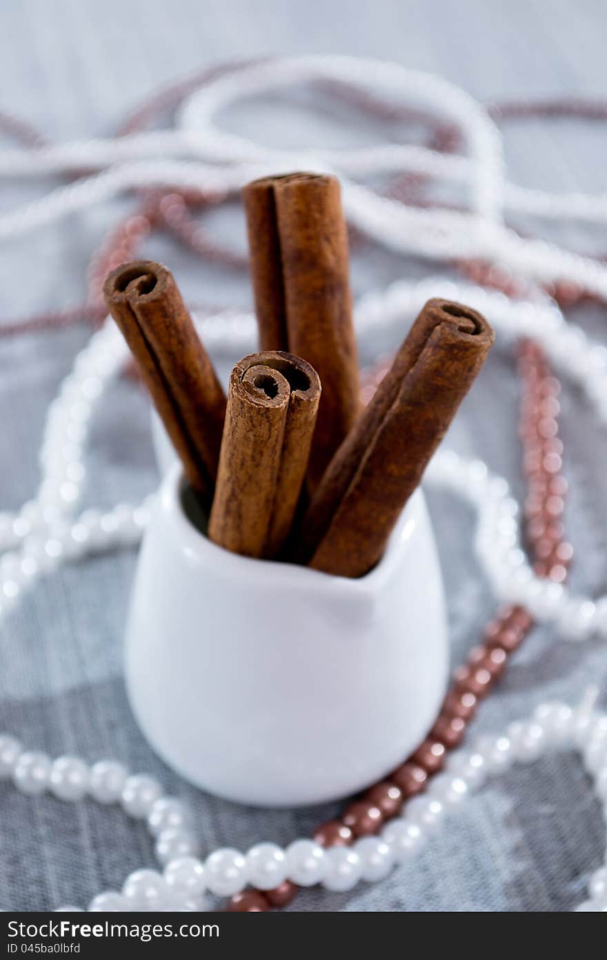 Cinnamon sticks in a white glass, beads on a blue background. Cinnamon sticks in a white glass, beads on a blue background