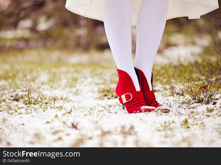 Part of feet in red shoes and white stockings on a grass and snow