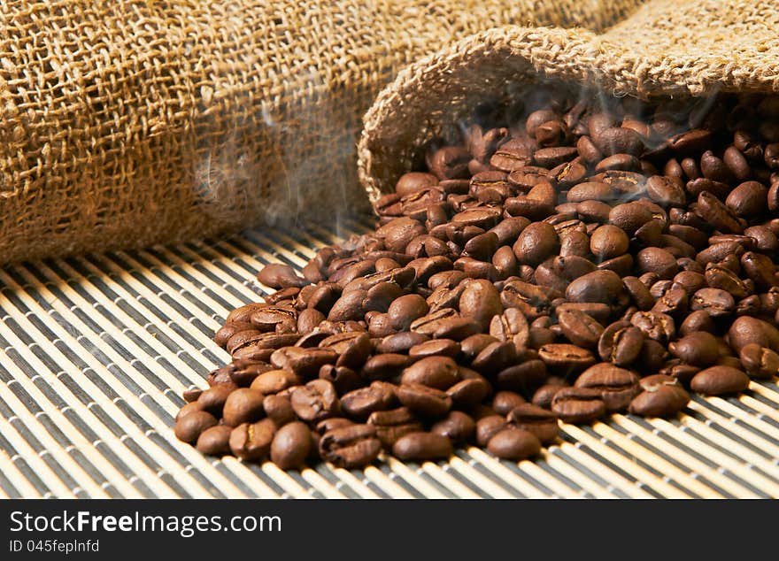 Fried grains of coffee with a smoke poured out a bag on a wooden napkin. Fried grains of coffee with a smoke poured out a bag on a wooden napkin