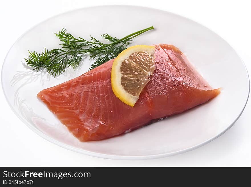 Fillet of red fish with a lemon and greens on a plate isolated on a white background