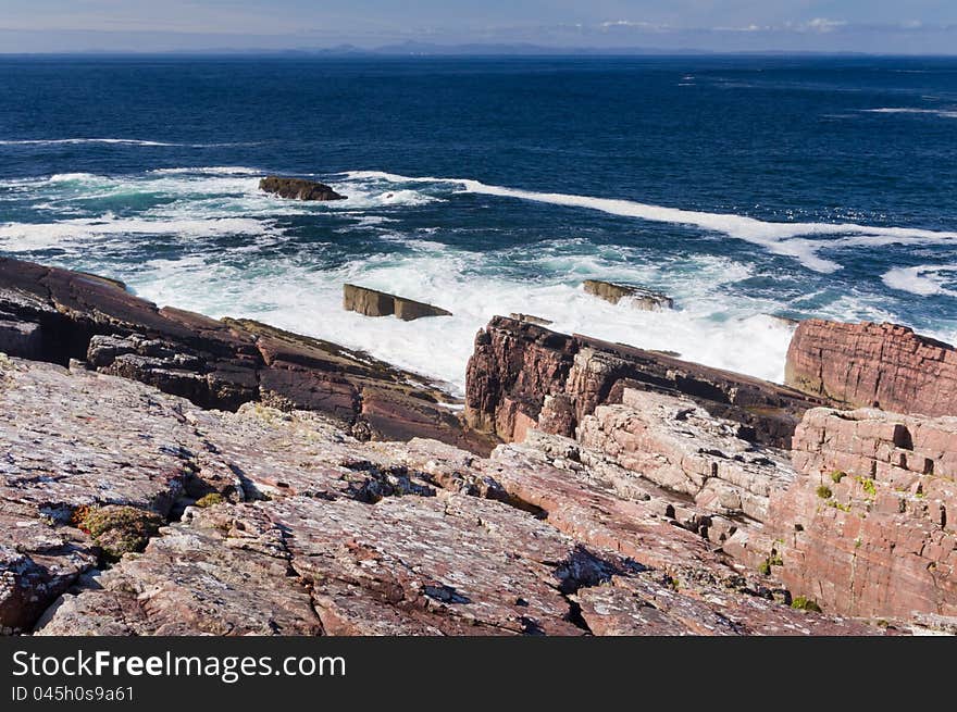 Granite entering the deep blue sea with a distant island on the horizon. Granite entering the deep blue sea with a distant island on the horizon