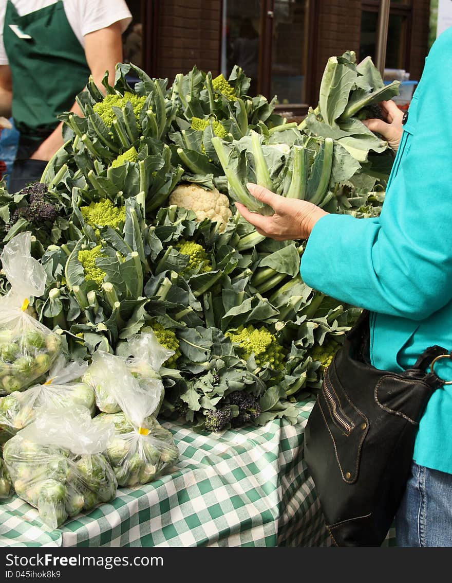 A mature female customer choosing and buying vegetables from a market stall. A mature female customer choosing and buying vegetables from a market stall