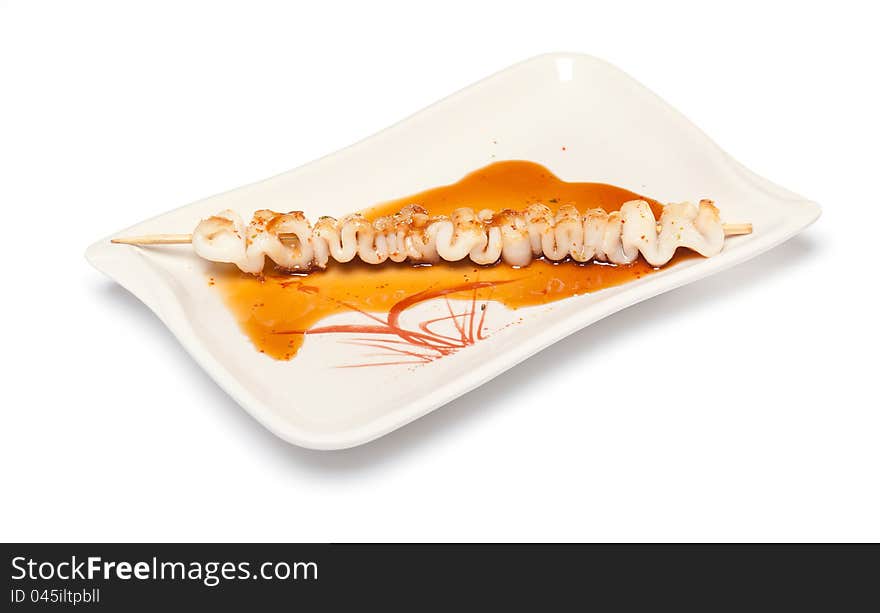 Skewered squid on wooden sticks grilled with sauce on a white plate on white background