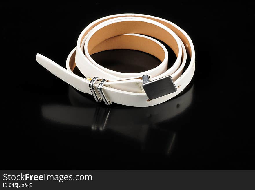 A women’s white leather belt with reflection on a black background. A women’s white leather belt with reflection on a black background